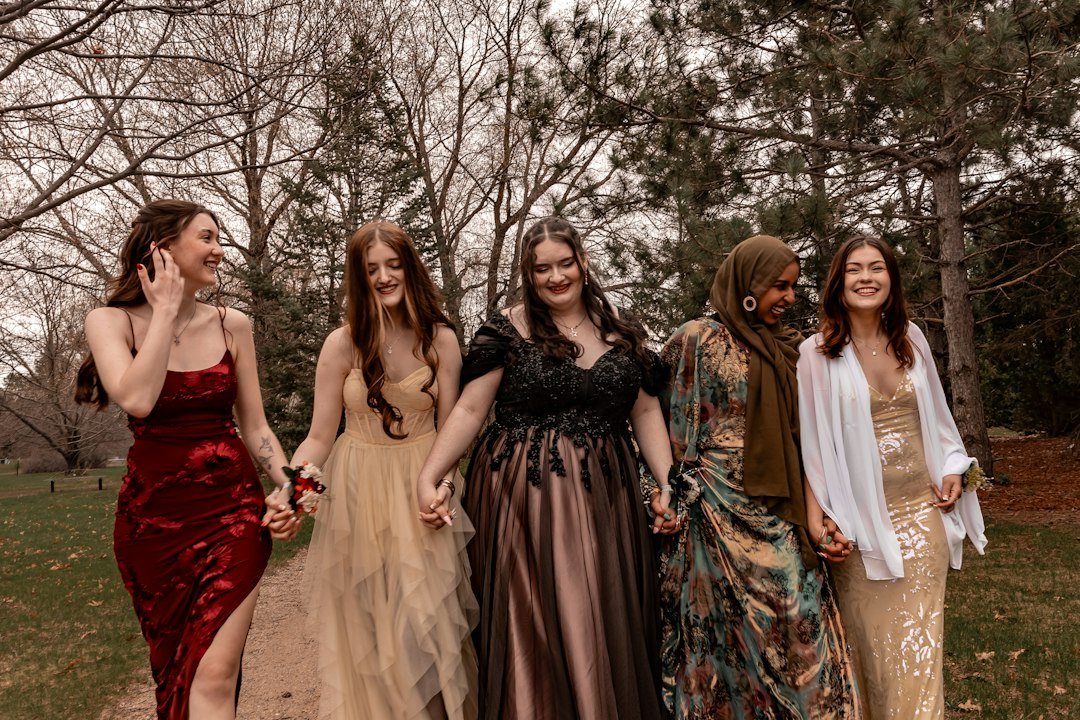 Gen Z slang - Five smiling women in formal dresses holding hands outdoors
