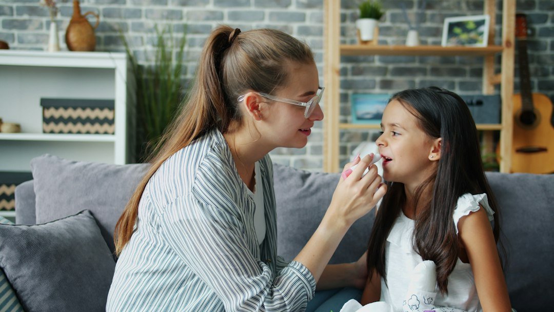 Parents and teens slang - Mother wiping daughter's nose with tissue on sofa